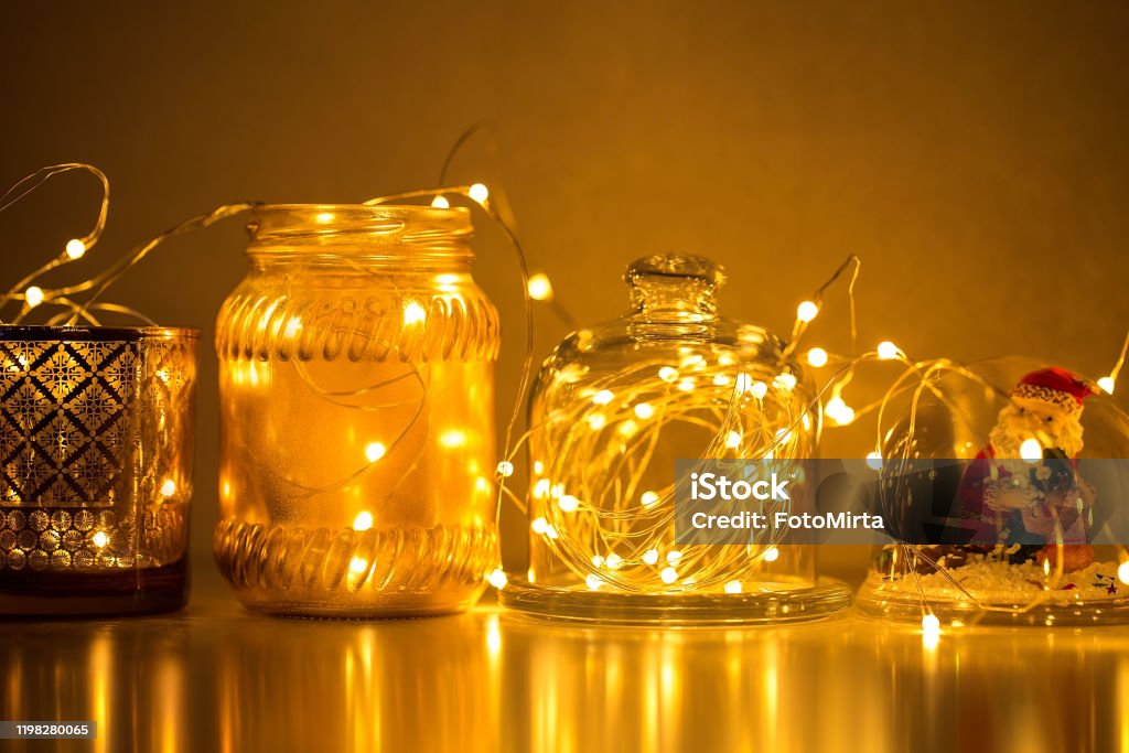 Garlands and decorations to create a cozy home, Golden lights on a wire, a candlestick, a vase, a snow glass ball and other decorations illuminated by lights. Garlands and decorations to create a cozy home, Golden lights on a wire, a candlestick, a vase, a snow glass ball and other decorations Christmas Lights Stock Photo
