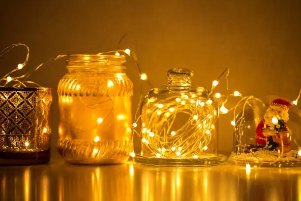 Photo of Garlands and decorations to create a cozy home, Golden lights on a wire, a candlestick, a vase, a snow glass ball and other decorations illuminated by lights.