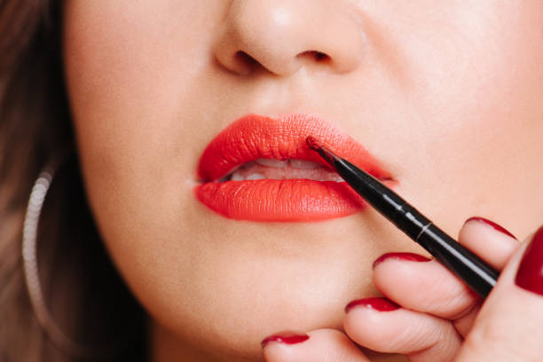 istock Stylist hand applying lipstick contour on a client's lips over yellow 1198283636