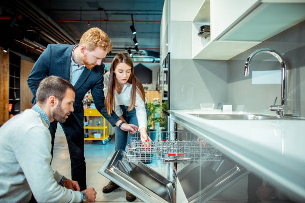 vendedor de la tienda que demuestra las características y funcionalidades de un lavavajillas a un joven esposo y esposa en una tienda de equipos de cocina - tienda de electrónica fotografías e imágenes de stock