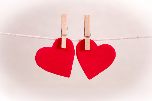 Valentine's Day Card. Two red hearts hung together with rustic string on a pale pink background with copyspace.