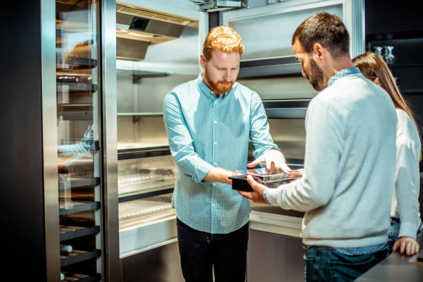 istock Store seller explaining the compartments usage in a new generation fridge to a young couple in a kitchen appliances store 1198290856