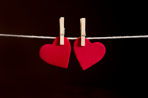 Valentine's Day card. Two red hearts hung together with rustic string on a dark background, with copyspace.