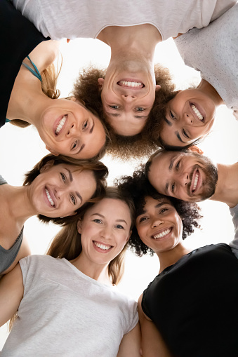 Low angle smiling diverse people standing in circle together, showing unity and support, young beautiful women and men looking at camera, motivated for teamwork success, starting training