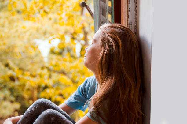 istock Sad young girl by the open Window looking outside 1198298215