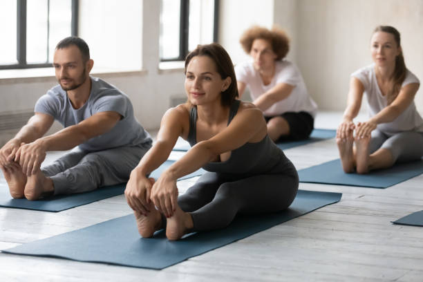 woman practicing yoga at group lesson, seated forward bend exercise - yin yang symbol fotos imagens e fotografias de stock