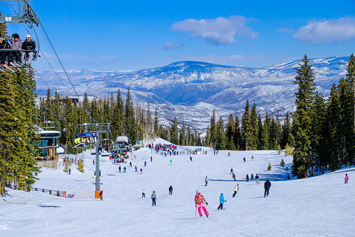 Beautiful view of Aspen Snowmass ski resort in Colorado, USA, on clear winter day; people skiing and snowboarding to base of chairlift; forest and mountains in background