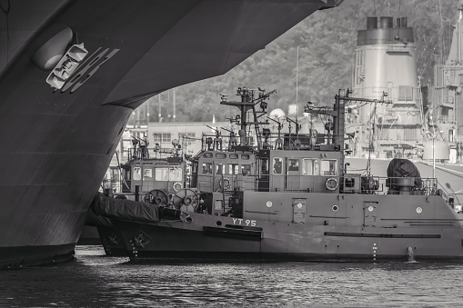 Yokosuka, Kanagawa / Japan - December 18, 2019:  Three tugs guide a Japan Maritime Self Defense Force ship toward its dock.