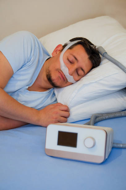 man wearing under the nose nasal mask ( CPAP mask ) and using CPAP machine for sleeping smoothly stock photo
