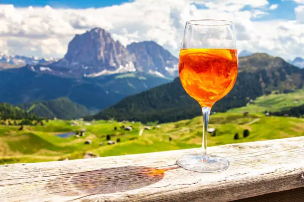 View of the traditional Italian alcoholic drink Spritz on the background of colorful Italian meadows and the Dolomites Alps mountains. village St. Cristina di Val Gardena Bolzano Seceda, Italy