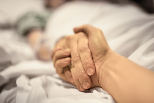 Man holding hand, giving support and comfort to woman, loved one sick in hospital bed.