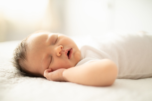 Baby with earring looking at camera reclining with a blanket on the bed. High quality photo