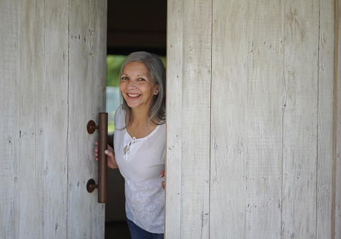 Portrait of beautiful senior woman opening the door to her home smiling at camera very cheerfully