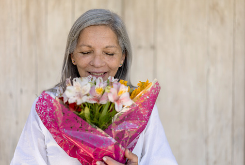 Happy senior woman smelling a beautiful flower bouquet with eyes closed - Headshot