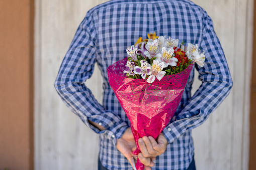 Close up of unrecognizable man holding a flower bouquet behind his back - Celebration concepts