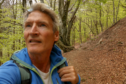 Mature man looks past camera while hiking in forest