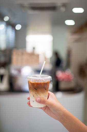 Female hand holding iced cafe latte in disposable take away cup