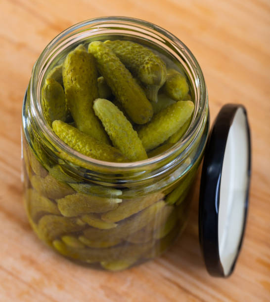 istock Opened glass jar with pickled cucumbers on wooden background 1198328307