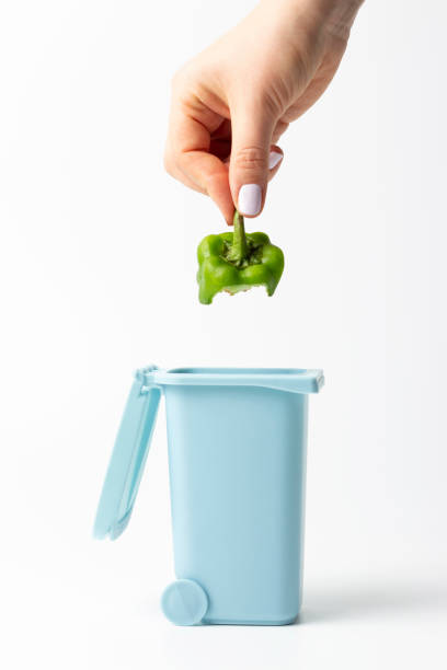Female hand throws food trash into trash can on white background