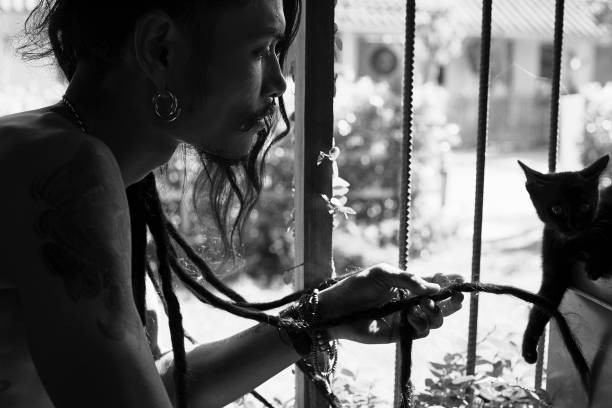 f stattlichen mann mit dunkler haut, tätowierung, piercing auf fit tan körper, dreadlocks, spielen mit kleinen schwarzen kätzchen. - sadness domestic cat black pensive stock-fotos und bilder