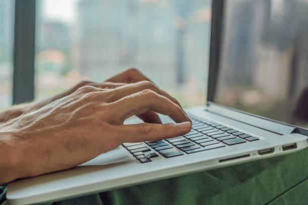 istock Young man is working on a laptop in his bed on a background of a panoramic window overlooking the skyscrapers. Freelancer, remote work, work from home 1198347265