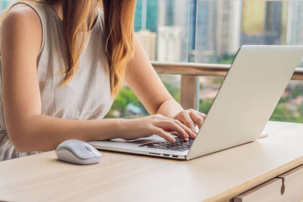 istock Young woman is working on a laptop on her balcony overlooking the skyscrapers. Freelancer, remote work, work from home 1198347300