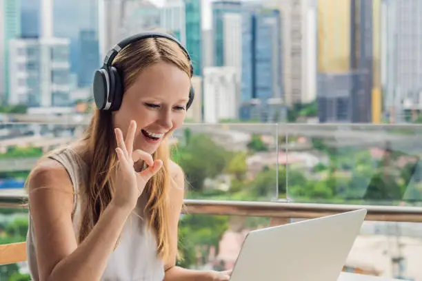 Photo of Young woman teaches a foreign language or learns a foreign language on the Internet on her balcony against the backdrop of a big city. Online language school lifestyle