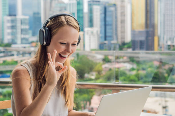 a mulher nova ensina uma língua extrangeira ou aprende uma língua extrangeira no internet em seu balcão de encontro ao contexto de uma cidade grande. estilo de vida da escola de línguas online - língua inglesa - fotografias e filmes do acervo