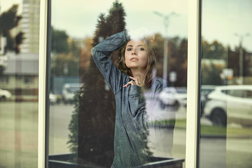 Woman young adult beautiful outside the window looking at the streets of the city through the glass