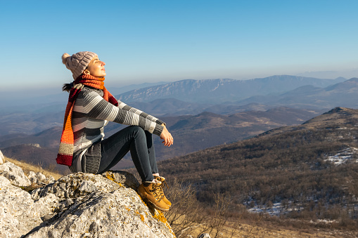 Woman sunbathing and meditating on top of the mountain on sunny winter day.