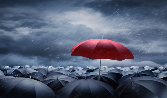 Crowd of black Umbrellas with one unique red outstanding umbrella in the storm