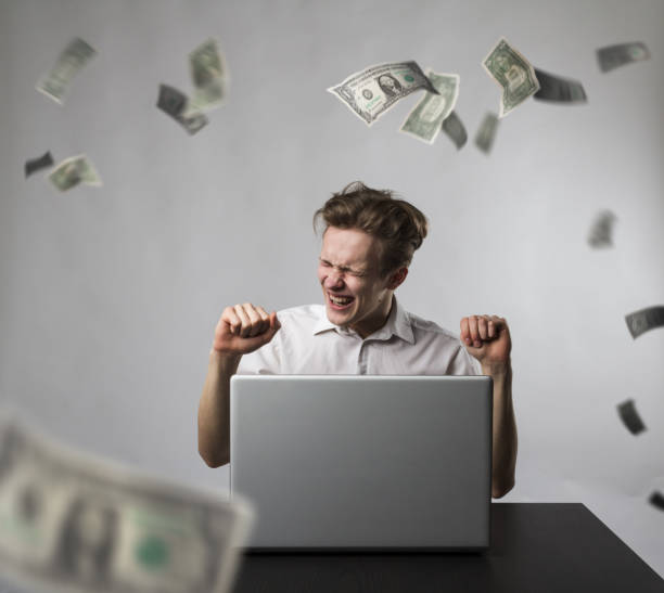 istock Young happy man with laptop and falling dollar banknotes. Success concept. 1198379949