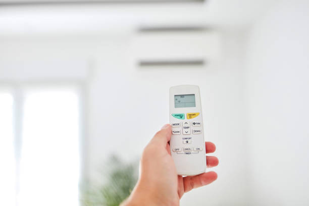 istock Modern air conditioner unit with a hand holding a remote. 1198385626