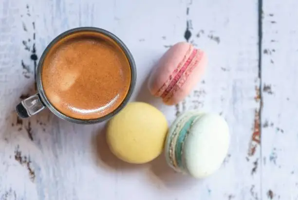 Macaron color pastel pink, yellow and mint top view copy space at right focus on top of glass of coffee.
