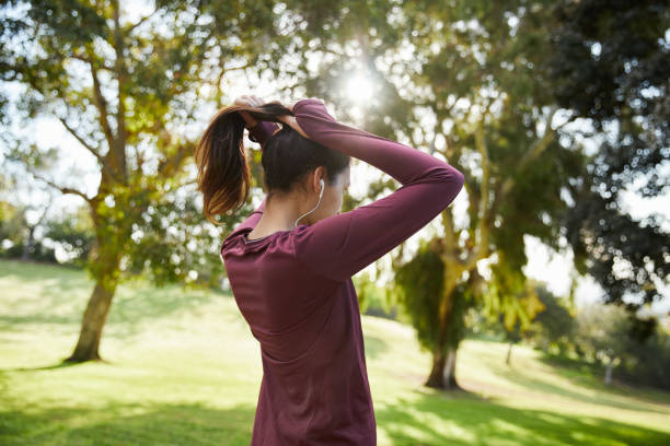 Fit young woman tying her hair back before a run Fit young woman in sportswear tying her hair back in a ponytail and listening to music on earphones before a run woman tying hair in ponytail getting ready for exercising stock pictures, royalty-free photos & images