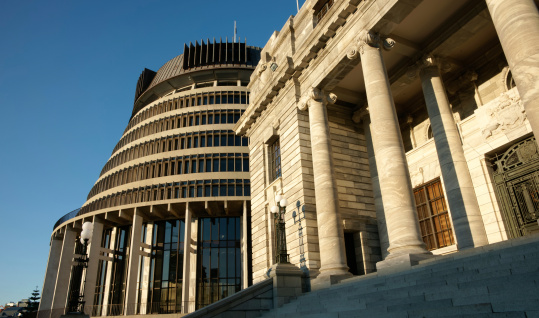 Contrasting architectural styles of Parliament Buildings, Wellington, New Zealand, inlcuding the circular colloquially known Beehive and the entrance and pillar at top of steps of parliament. Low angle view.