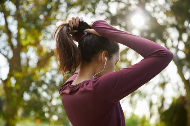 Fit young woman in sportswear listening to music on earphones and tying her hair back in a ponytail before a run
