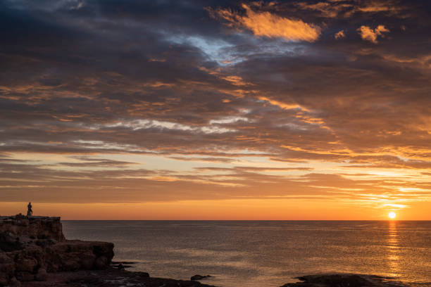 istock Silhouette of a lonely man who is sitting and looking at sunrise / sunset on dramatic sky 1198394251