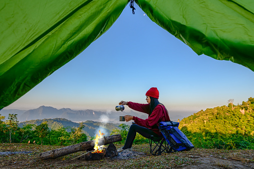 view of tent of woman traveller enjoy hot drink in front of living tent, prepare hot drink in the morning, wild and adventure trip of alone woman