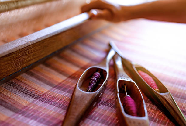 istock Woman working on weaving machine for weave handmade fabric. Textile weaving. Weaving using traditional hand weaving loom on cotton strands. Textile or cloth production in Thailand. Asian culture. 1198398707