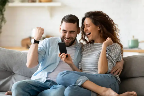 Photo of Excited couple holding smartphone celebrating online lottery win