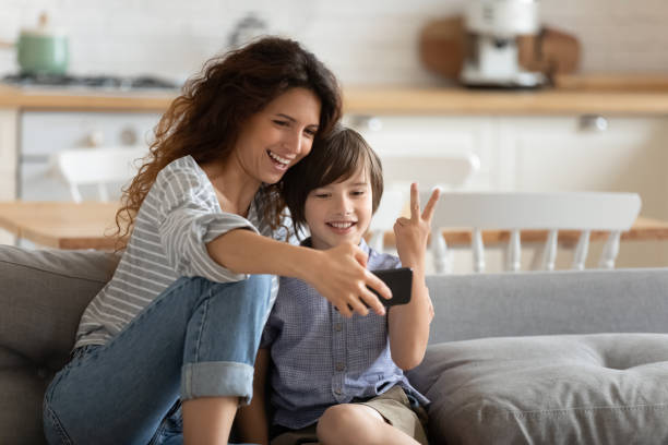 Cheerful mother holding smartphone making selfie with son