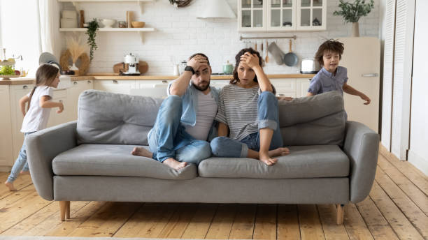 eltern müde von lauten kindern, die laufen und schreien - family sofa men sitting stock-fotos und bilder