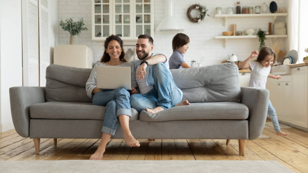 tandis que les enfants actifs exécutant des parents se reposant sur le sofa utilisant l'ordinateur portatif - domestic life photos et images de collection