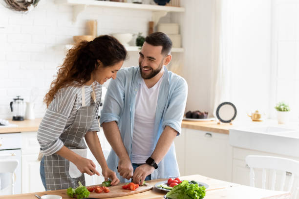 Couple preparing together vegetable salad standing in kitchen at home Happy couple standing in kitchen at home preparing together yummy dinner on first dating, spouses chatting enjoy warm conversation and cooking process, caring for health, eating fresh vegetable salad wife stock pictures, royalty-free photos & images