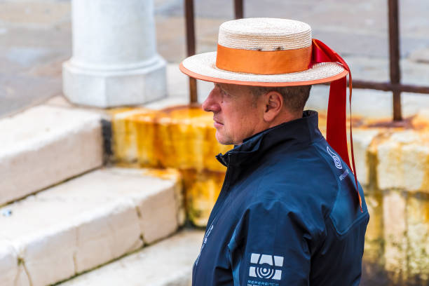 atractivo gondolero italiano de mediana edad / remansman / barquero que lleva sombrero de barador de paja duro con cinta roja y chaqueta de lluvia negro / azul marino. sin expresión facial. - oarsman sport nautical vessel one person fotografías e imágenes de stock