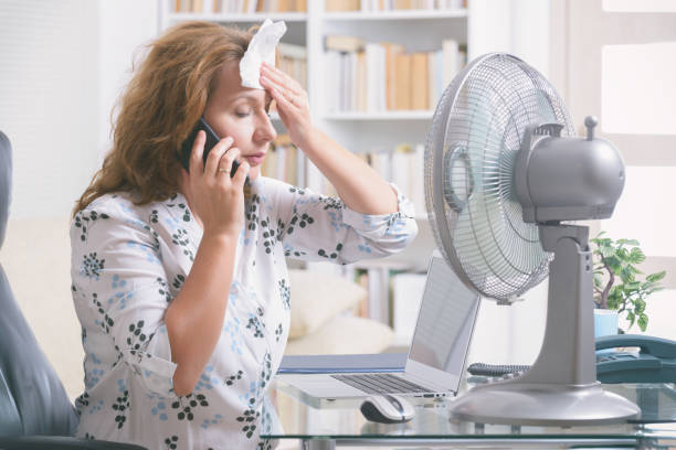 женщина страдает от жары в офисе или дома - office fan стоковые фото и изображения