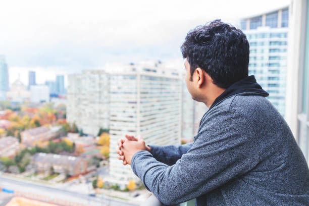 Young man newly immigrated to Canada admiring views from his apartment balcony of a highrise Asian, Admiration, Real People - Asian man admiring views from a high-rise expatriate photos stock pictures, royalty-free photos & images