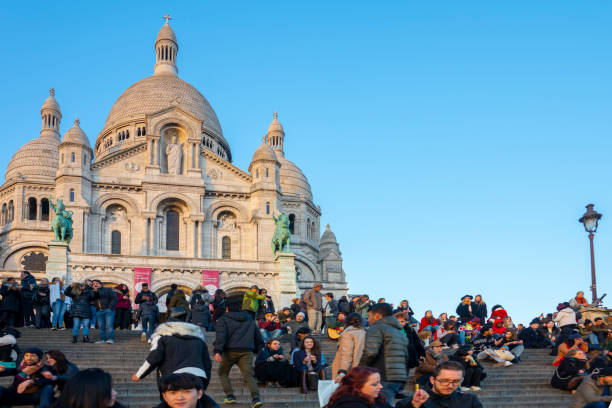 Paris Montmartre with hundreds of tourists on the stairs in front of the Cathedral looking at the sunset over Paris, France they are in front of the Cathedral. In Paris, France.
