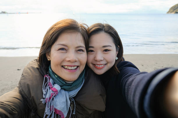 Active mature woman and her daughter taking selfie on beach POV of active mature woman and her daughter taking selfie on beach photographing herself stock pictures, royalty-free photos & images